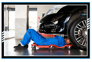 Mechanic in blue uniform lying down and working under car at auto service garage